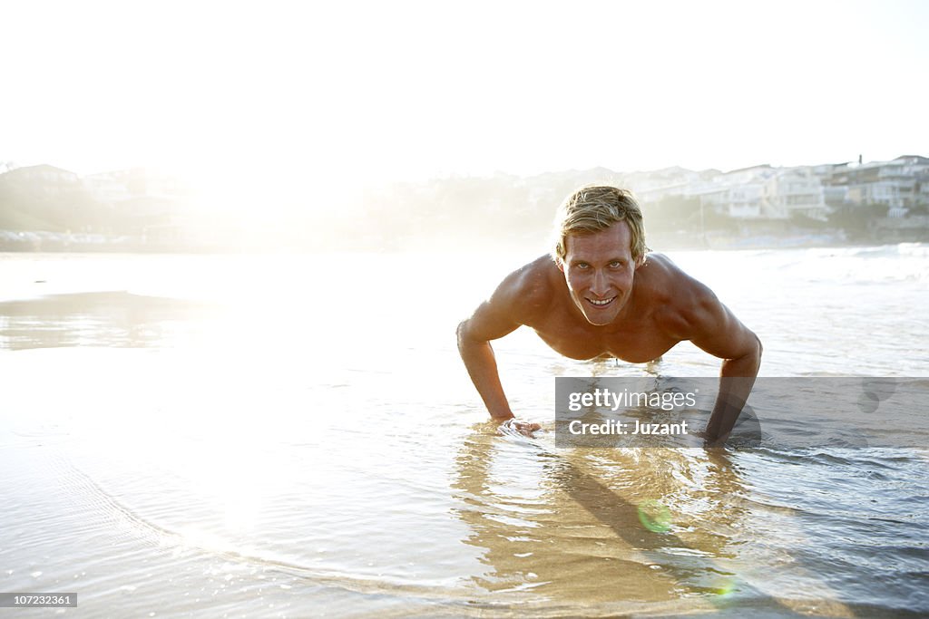 Young man doing press up in the water at beach