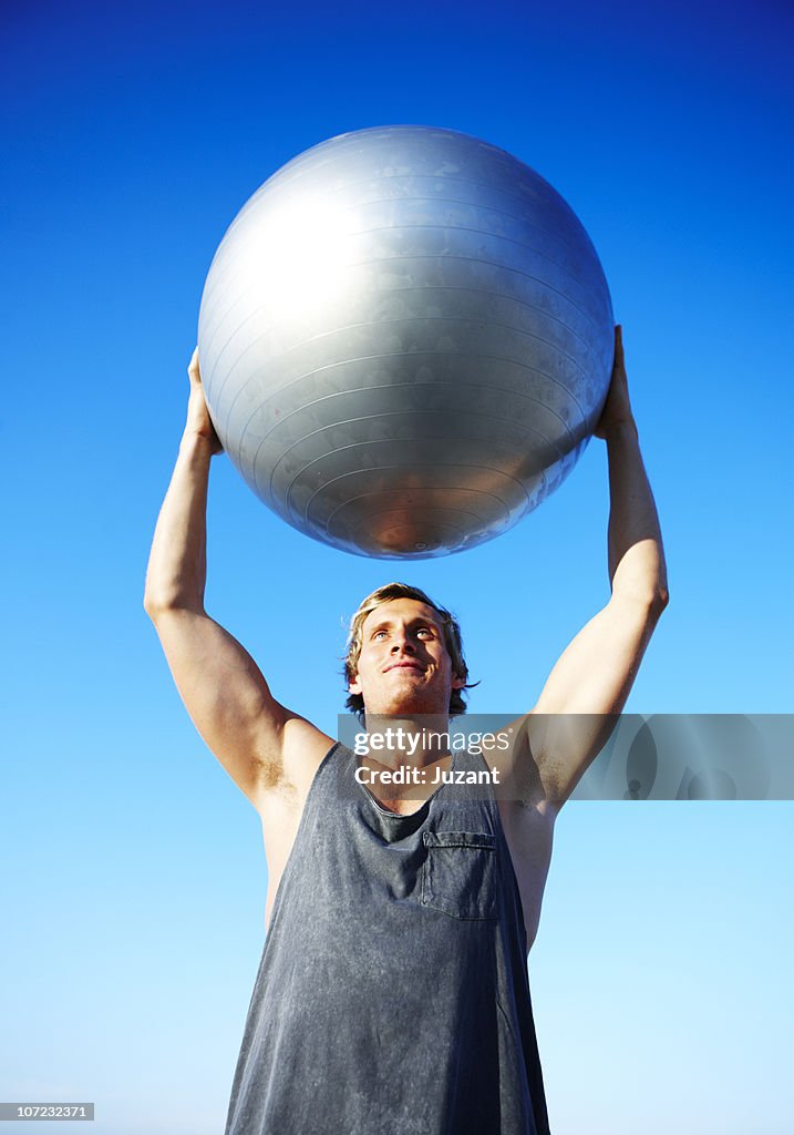 Young man holding exercise ball over his head