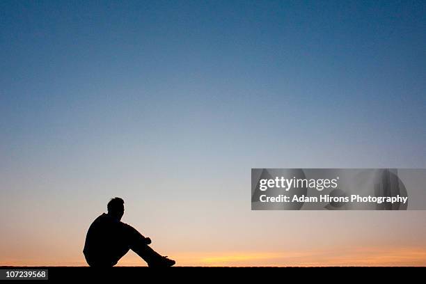 silhouette man sitting at sunset - hand op knie stockfoto's en -beelden