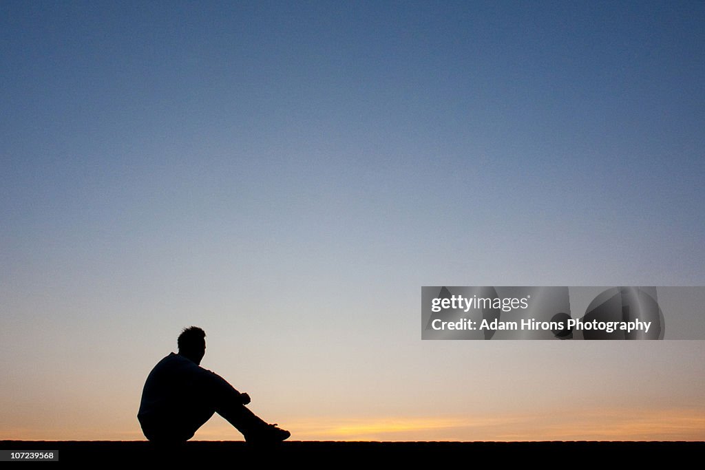 Silhouette man sitting at sunset