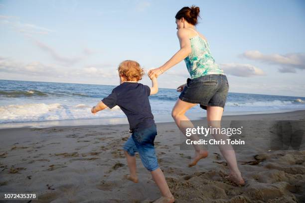 mother and child running hand in hand towards the water at the beach - mother and child in water at beach stock pictures, royalty-free photos & images