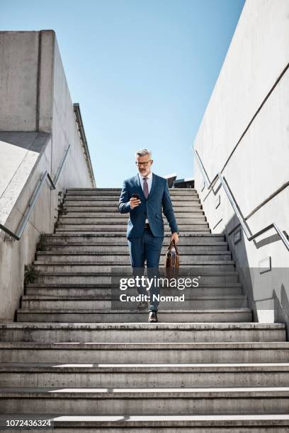 empresario mediante teléfono móvil sobre las medidas en la ciudad de - business man walking fotografías e imágenes de stock