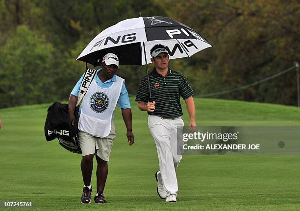 Britain's Louis Oosthuizen and his caddie take cover from the rain under an umbrella during day one of the South African Nedbank Golf Challenge in...