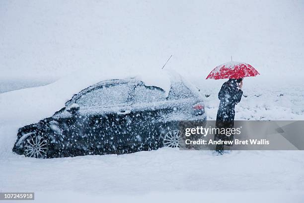 woman on mobile alongside car in a snow drift - schneesturm stock-fotos und bilder