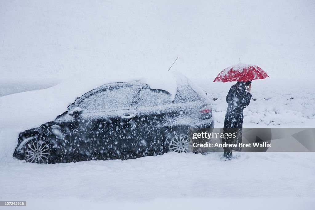 Woman on mobile alongside car in a snow drift