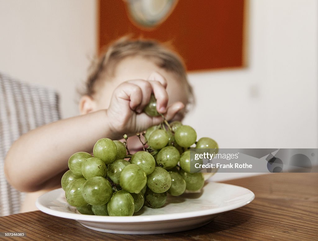 Young girl catchs a grape from a plate