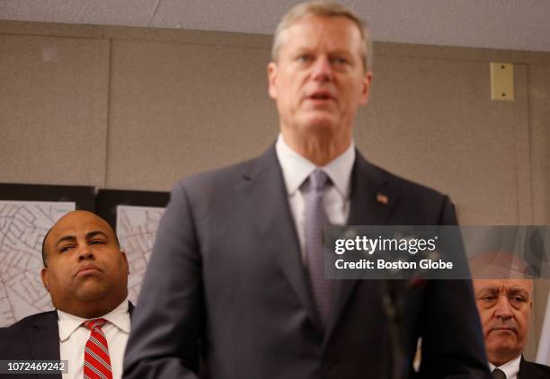 Lawrence Mayor Dan Rivera, left, and North Andover town manager Andrew Maylor, right, listen as Massachusetts Governor Charlie Baker speaks at a...