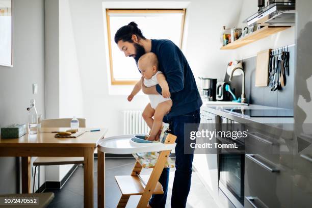 single father putting baby in high chair - high chair stock pictures, royalty-free photos & images