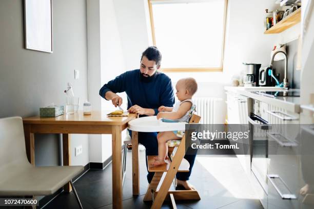 single father feeding baby in high chair - high chair stock pictures, royalty-free photos & images