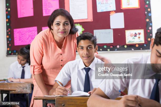 female student with teacher in classroom writing in notebook - stock image - indian tour guide stock pictures, royalty-free photos & images