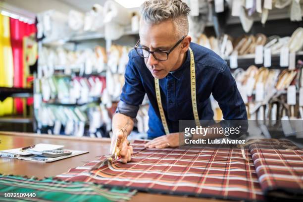 male tailor cutting a textile at workbench - entrepreneur manufacturing stockfoto's en -beelden