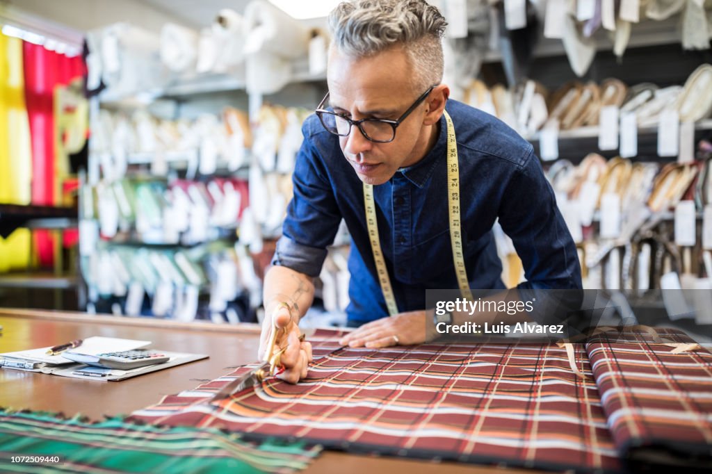 Male tailor cutting a textile at workbench