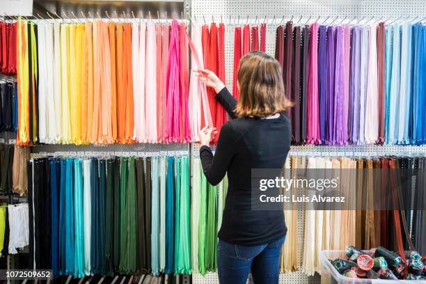 woman examining colorful zippers on rack in store - vestido feito à medida - fotografias e filmes do acervo