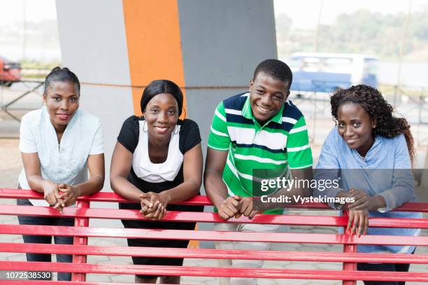 this group of young friends in a park leaning on a bench with a beautiful smile. - costa de marfil fotografías e imágenes de stock