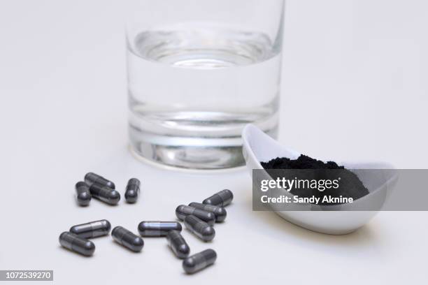 close up of a box of activated charcoal capsules and powder with a glass of water. - activated charcoal capsule stock pictures, royalty-free photos & images