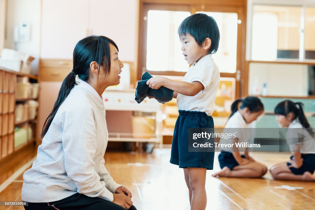 Young boy showing his folded uniform to his teacher at preschool