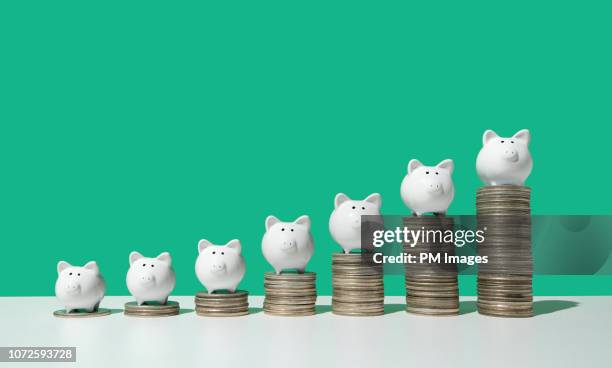 little piggy banks on ascending stacks of coins - saving photos et images de collection