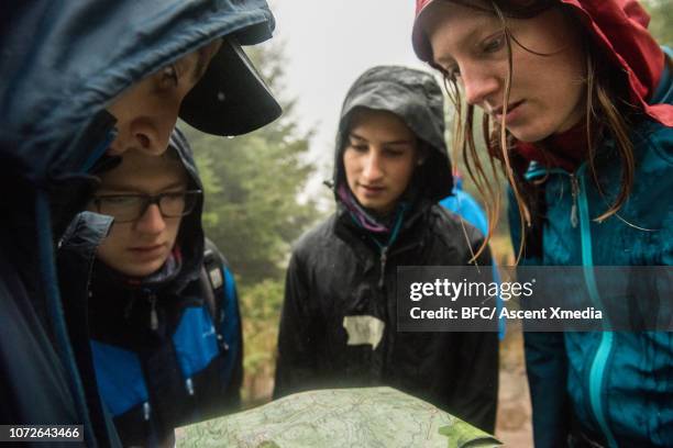 young adults orienteering with map in rain - orientierungslauf landkarte gruppe stock-fotos und bilder