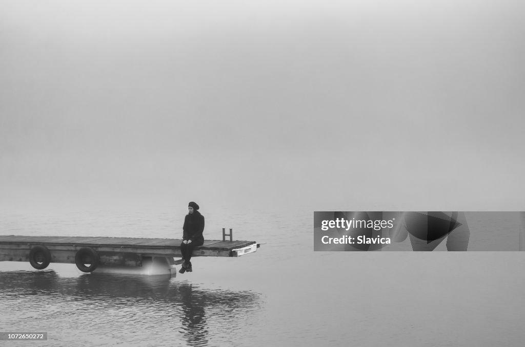 Lonely sad woman sitting on the wooden dock