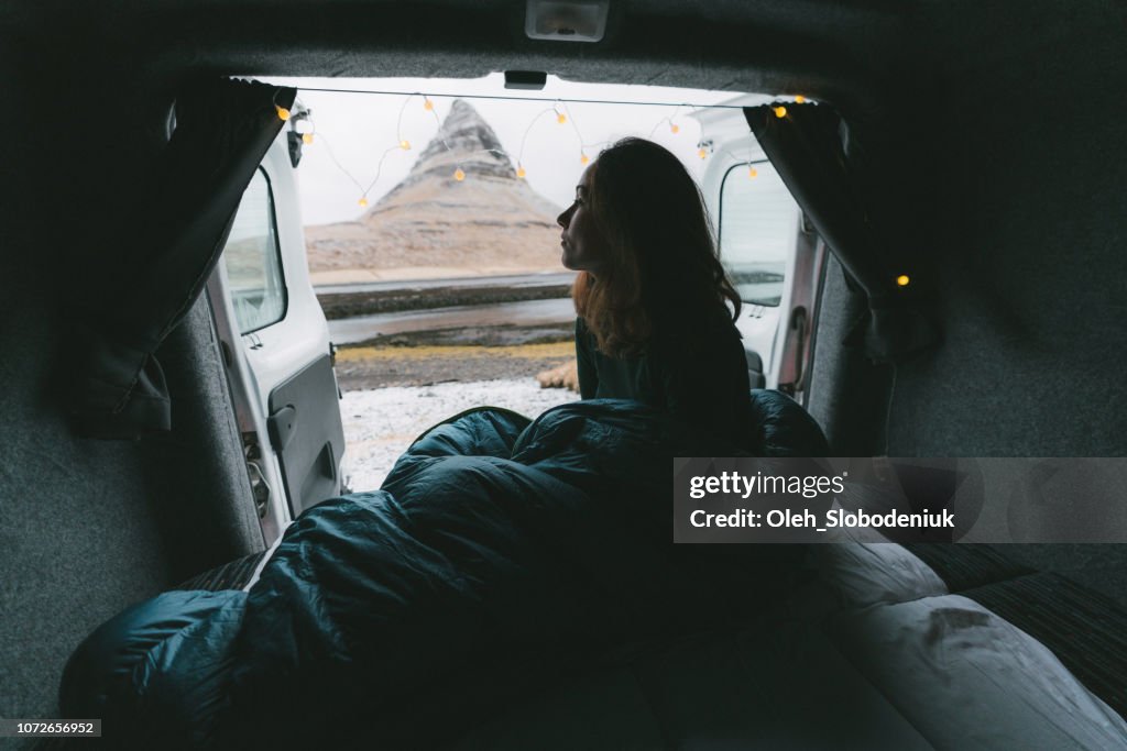 Donna in sacco a pelo guardando la montagna Kirkjufell dal camper