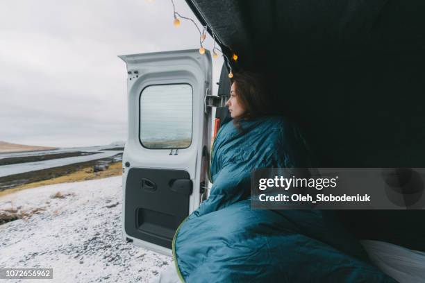 woman in sleeping bag looking at kirkjufell mountain from camper van - motor home winter stock pictures, royalty-free photos & images