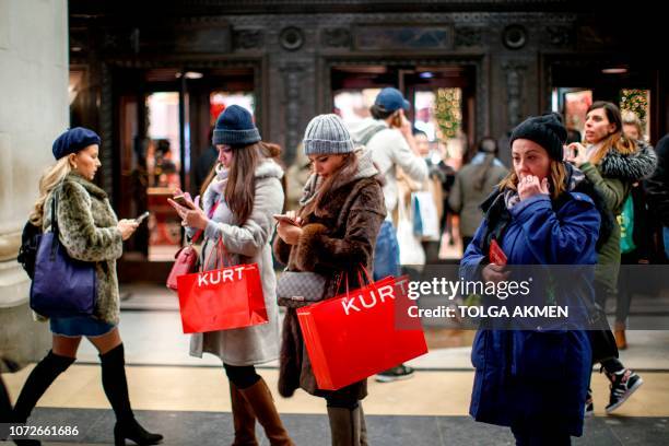 Shoppers carry purchases as they look at their smartphones on the main shopping district on Oxford Street in London on December 13, 2018 less than...