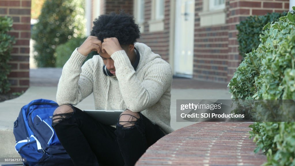Male college student rests head in hands while sitting on staircase