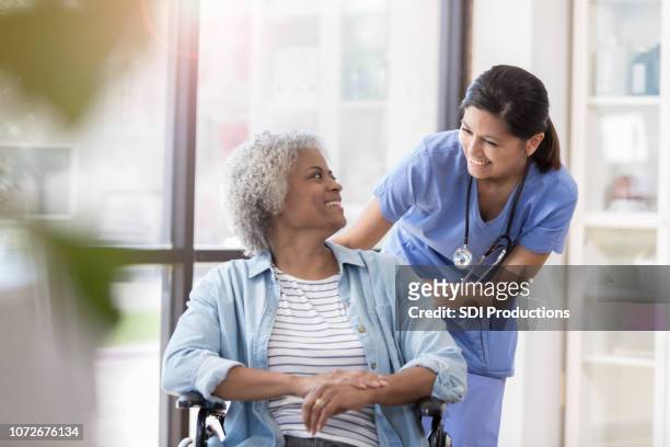 nurse pushes female patient in wheelchair - nurse candid stock pictures, royalty-free photos & images