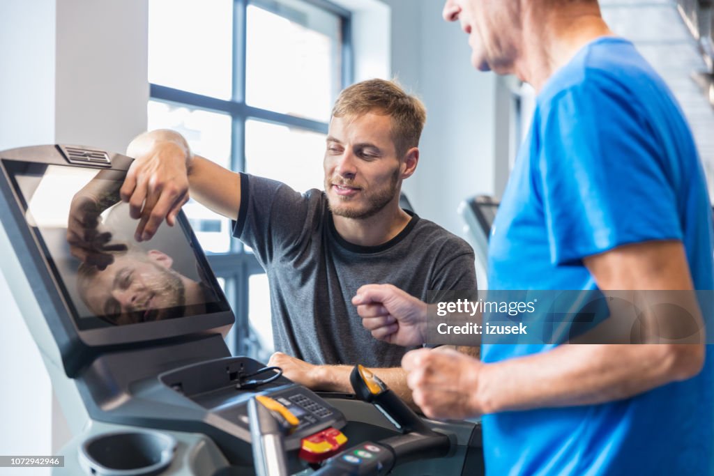 Trainer supervising old man on treadmill