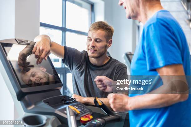 trainer supervising old man on treadmill - rehabilitation stock pictures, royalty-free photos & images