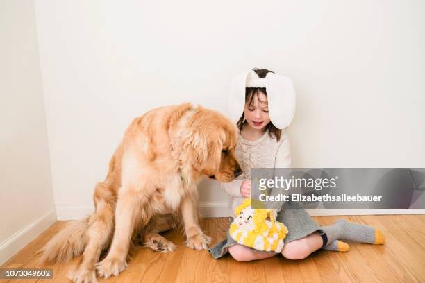 girl wearing bunny ears sitting on floor playing with her dog - dog easter stock-fotos und bilder