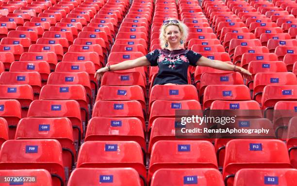 smiling woman with her arms outstretched sitting in an empty stadium - liberty stadion stock pictures, royalty-free photos & images