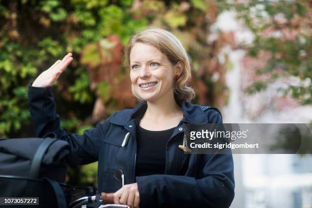 woman standing with her bicycle waving - woman waving goodbye photos et images de collection