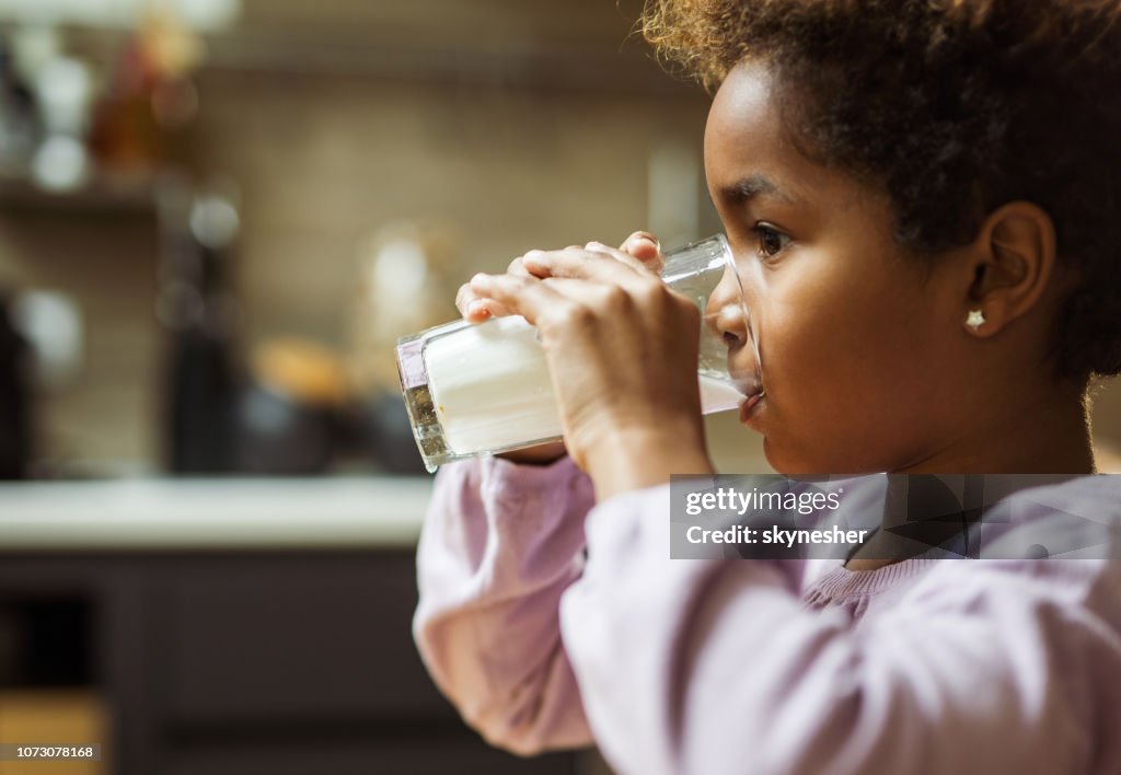 Profile view of small black girl drinking milk at home.