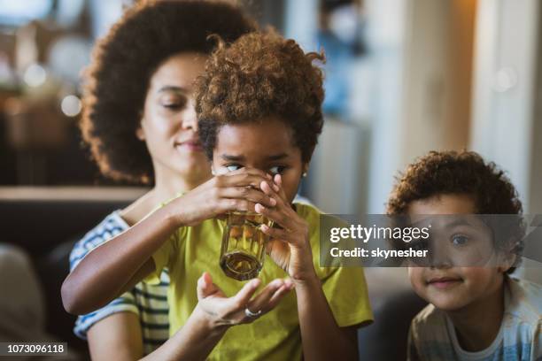pequeña muchacha afroamericana agua potable con ayuda de su madre. - niño-tomando-agua fotografías e imágenes de stock
