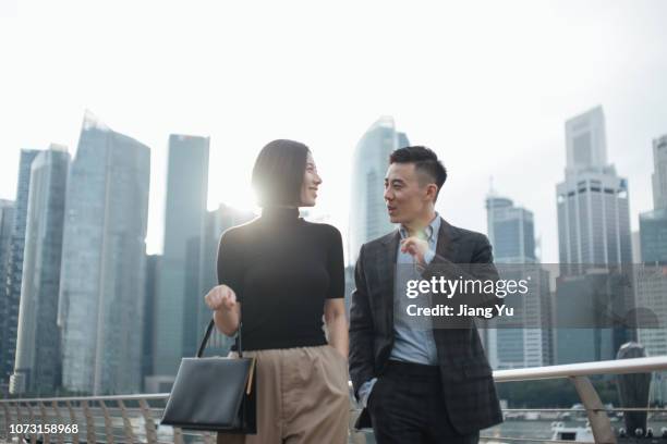 successful young couple talking to each other and walking against urban cityscape in singapore - wealthy asian man stock pictures, royalty-free photos & images