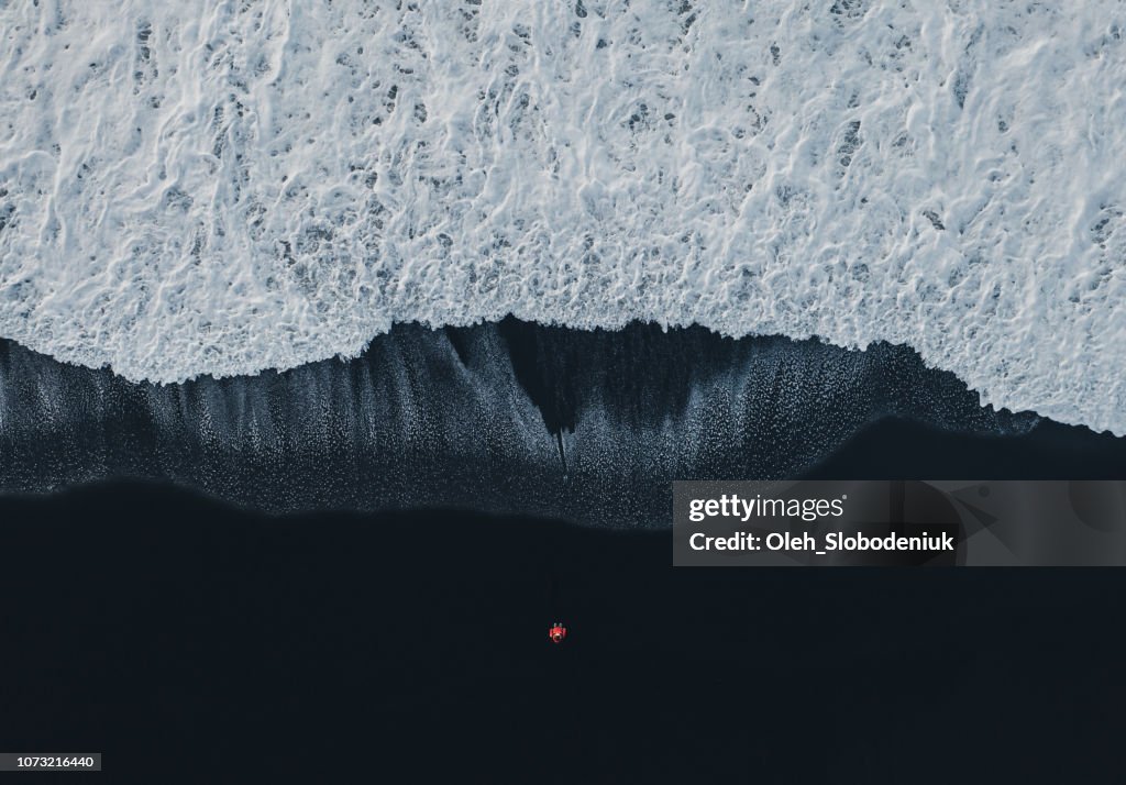 Vista aérea de la mujer en la playa de arena negra en Islandia