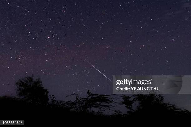 This photo taken late December 14, 2018 with a long time exposure shows a meteor streaking through the night sky over Myanmar during the Geminid...