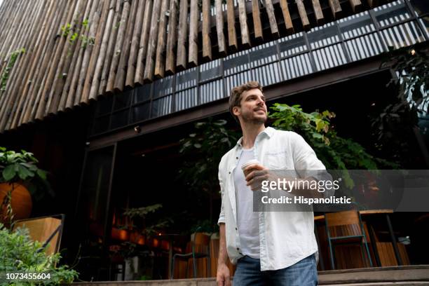 cheerful latin american guy leaving a coffee shop looking away smiling - leaving restaurant stock pictures, royalty-free photos & images