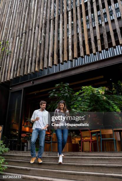 cheerful young couple leaving a coffee shop with a take out coffee talking and having fun - couple restaurant stock pictures, royalty-free photos & images