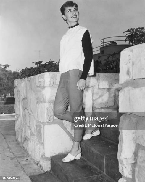 Belgian-born actress Audrey Hepburn , circa 1955. She is wearing capri pants and a white tunic with black sleeves.