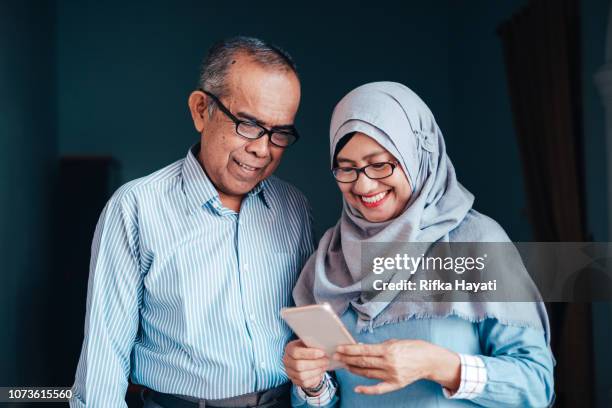 senior aziatische paar kijken naar smartphone - indonesische etniciteit stockfoto's en -beelden
