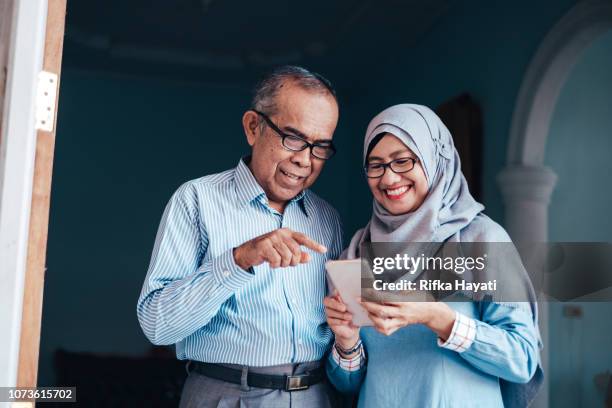 senior asian couple looking at smartphone - indonesian ethnicity stock pictures, royalty-free photos & images