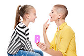 Cute young girl with speech therapist practicing correct pronunciation. Child speech therapy concept on white background. Speech impediment corrective exercises.