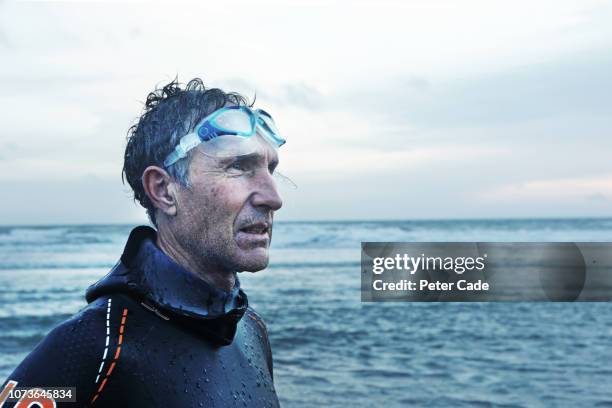 older man stood on beach after swimming in the sea - senior athlete stock pictures, royalty-free photos & images