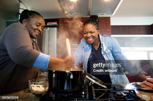 mother and daughter preparing traditional pap together in a kitchen gas stove - south african culture stock pictures, royalty-free photos & images