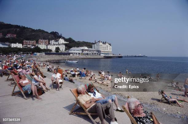 Holiday makers soak up the sun relaxing in deckchairs on the coast of seaside resort Llandudno, between Bangor and Colwyn Bay, Wales, June 1982.