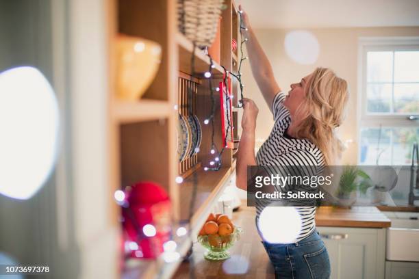 mature woman reaching high to hang lights - hanging christmas lights stock pictures, royalty-free photos & images