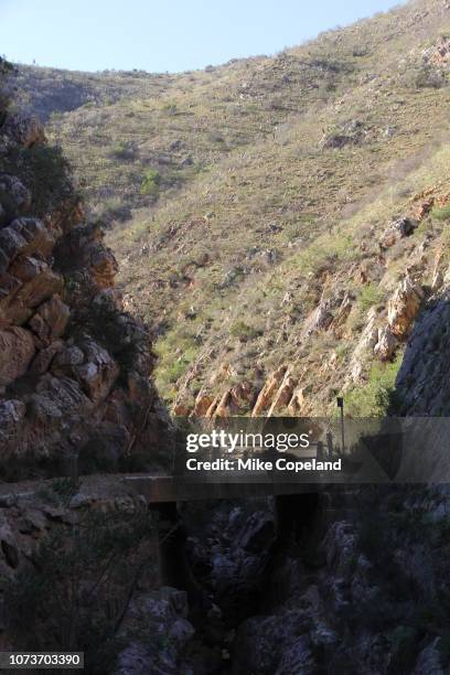 a bend in the narrow, winding gravel road on a rocky corner crosses a bridge in a kloof on prince alfred's pass through the outeniqua mountains between knysna and avontuur in the western cape province of south africa. - avontuur foto e immagini stock