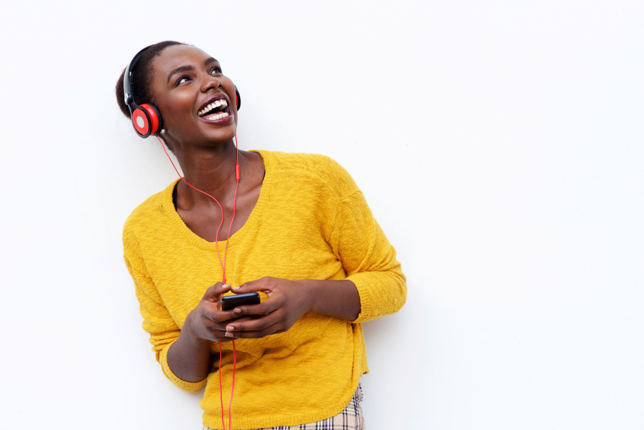 smiling young african woman listening to music with headphones and mobile phone against isolated white background smiling young african woman listening to music with headphones and mobile phone against isolated white background